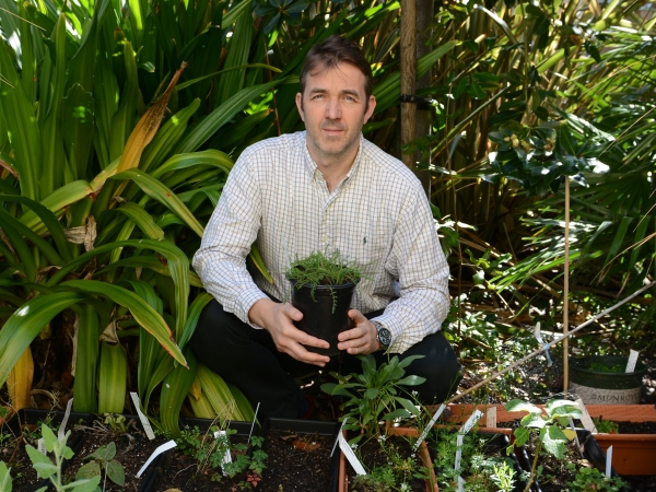 Geoffrey Abbott sits in a garden holding a potted plant